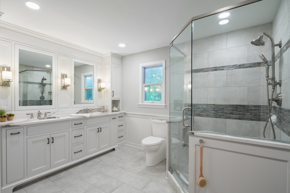 This is an example of a large transitional master bathroom in Columbus with shaker cabinets, grey cabinets, a corner shower, a one-piece toilet, grey walls, marble floors, an undermount sink, engineered quartz benchtops, grey floor, a hinged shower door, multi-coloured benchtops, a double vanity and a built-in vanity.