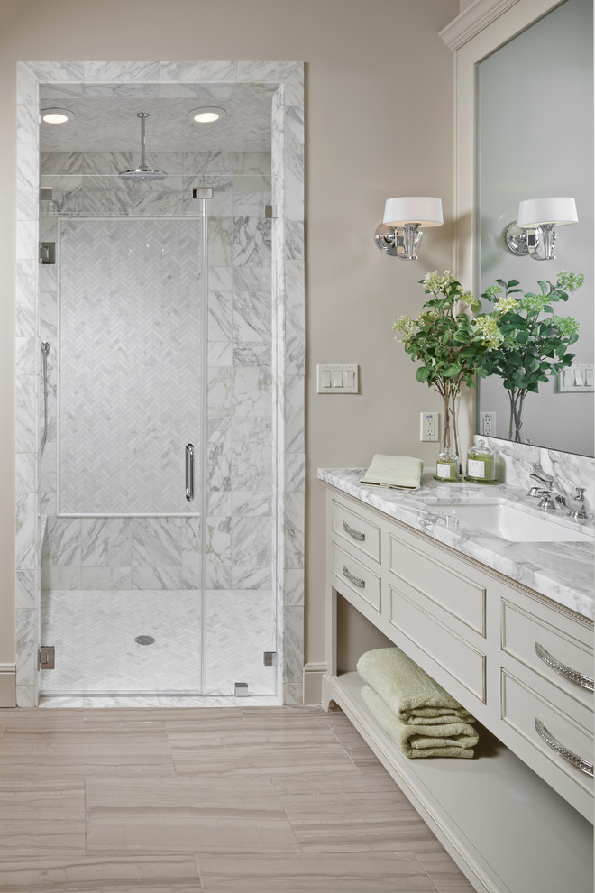 Inspiration for a large traditional master bathroom in Dallas with an alcove shower, beige cabinets, gray tile, white tile, beige walls, porcelain floors, an undermount sink, marble benchtops, marble, beige floor, a hinged shower door and recessed-panel cabinets.