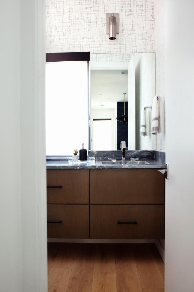 Photo of a mid-sized modern powder room in Austin with flat-panel cabinets, dark wood cabinets, white walls, medium hardwood floors, an undermount sink, marble benchtops, grey benchtops, a built-in vanity and wallpaper.