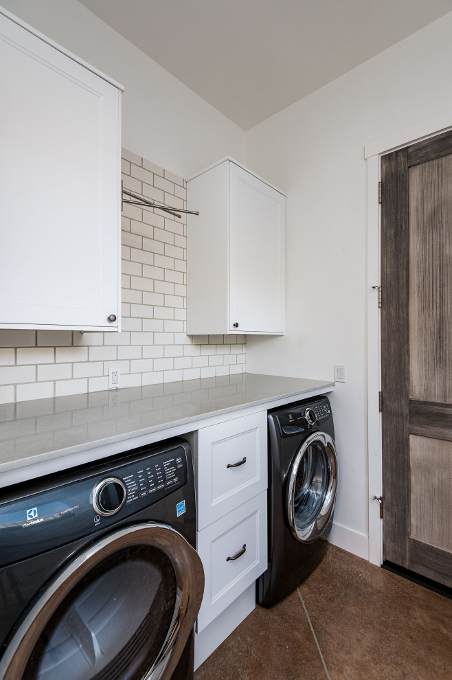 Inspiration for a large galley utility room in Portland with shaker cabinets, white cabinets, solid surface benchtops, grey splashback, stone slab splashback, white walls, concrete floors, a concealed washer and dryer, brown floor and grey benchtop.