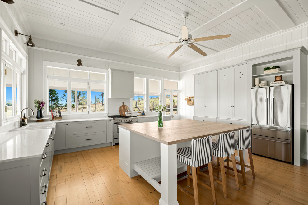 Mid-sized country l-shaped kitchen pantry in Sunshine Coast with a farmhouse sink, shaker cabinets, green cabinets, quartz benchtops, white splashback, engineered quartz splashback, stainless steel appliances, medium hardwood floors, with island, yellow floor, white benchtop and timber.