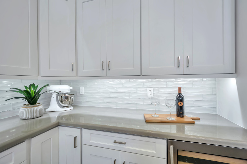 Example of a large transitional u-shaped porcelain tile, beige floor and exposed beam enclosed kitchen design in Phoenix with a farmhouse sink, shaker cabinets, white cabinets, quartz countertops, white backsplash, glass tile backsplash, stainless steel appliances, an island and white countertops