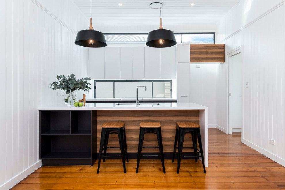 Mid-sized contemporary galley open plan kitchen in Brisbane with an undermount sink, flat-panel cabinets, white cabinets, quartz benchtops, glass sheet splashback, medium hardwood floors and with island.