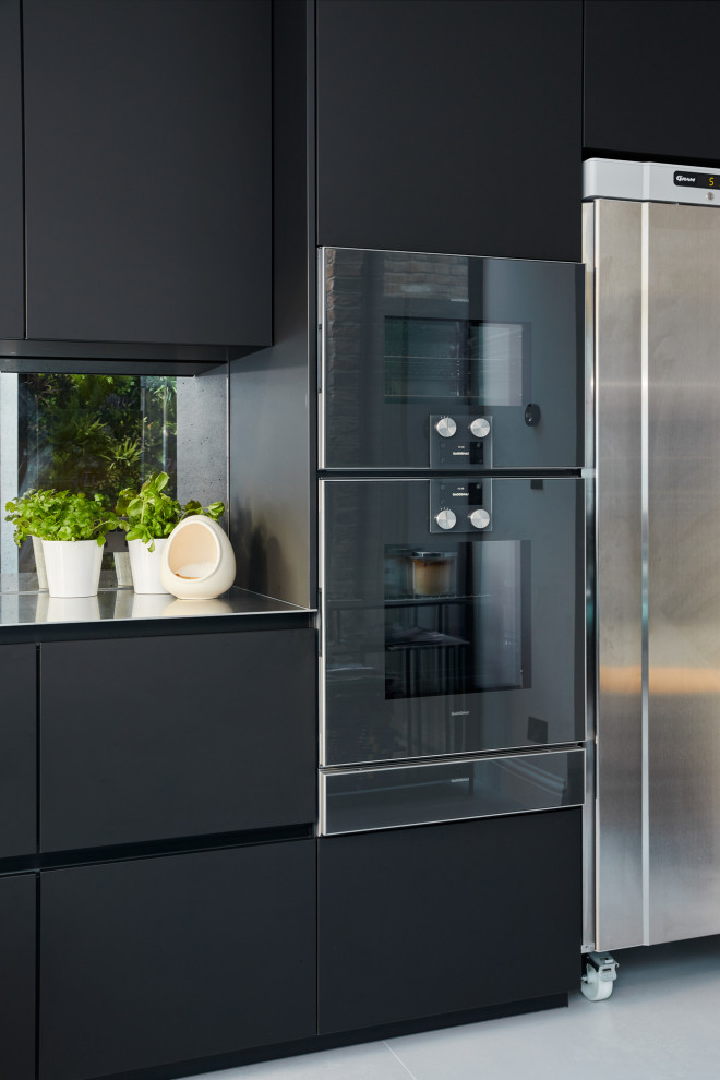 Small modern single-wall kitchen/diner in London with flat-panel cabinets, black cabinets, stainless steel worktops and an island.