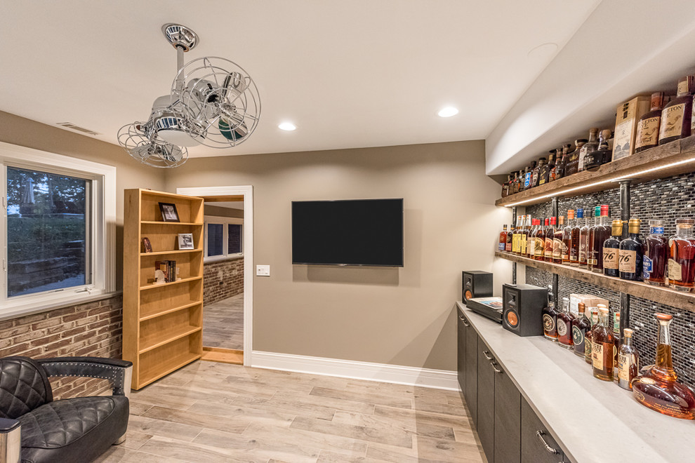 Mid-sized industrial single-wall wet bar in Chicago with an undermount sink, flat-panel cabinets, dark wood cabinets, metal splashback, light hardwood floors and beige floor.