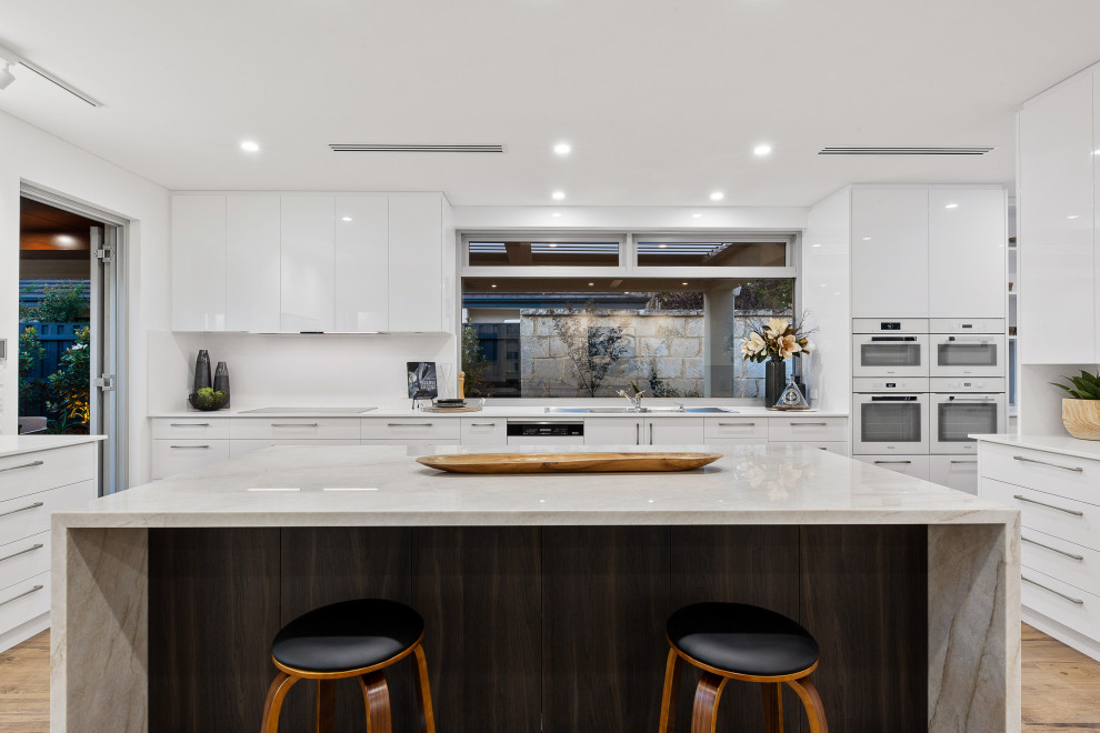 Inspiration for a large contemporary u-shaped kitchen in Perth with a double-bowl sink, flat-panel cabinets, white cabinets, white splashback, medium hardwood floors, with island, beige floor and white benchtop.