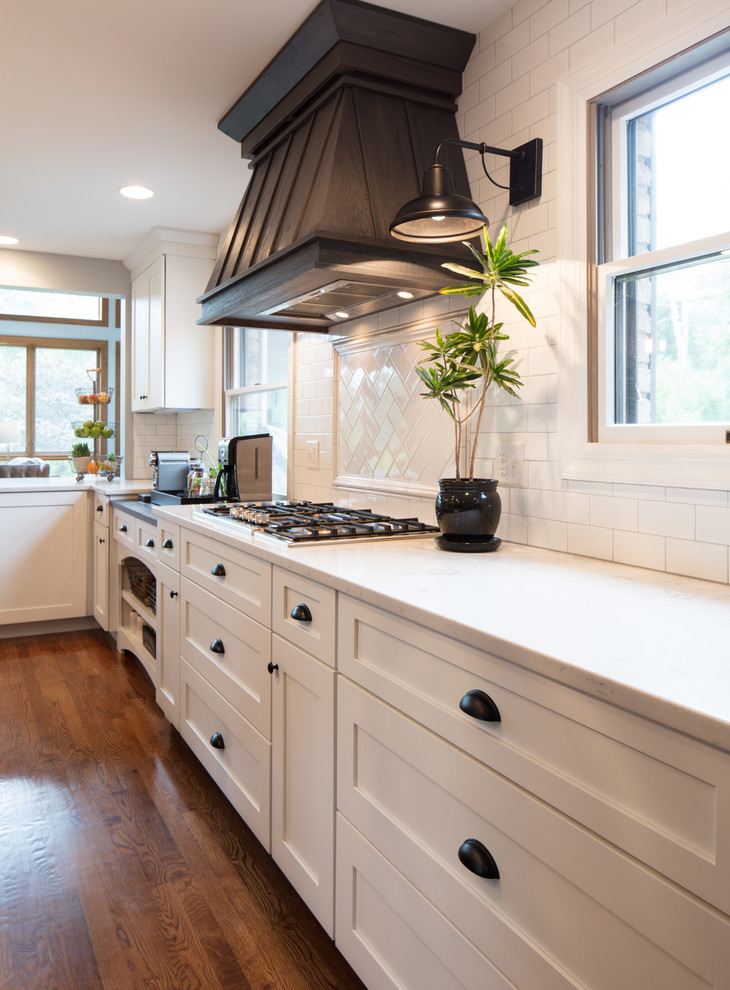 Inspiration for a mid-sized country u-shaped eat-in kitchen in Cincinnati with an undermount sink, shaker cabinets, white cabinets, quartz benchtops, white splashback, subway tile splashback, stainless steel appliances, medium hardwood floors, with island and brown floor.