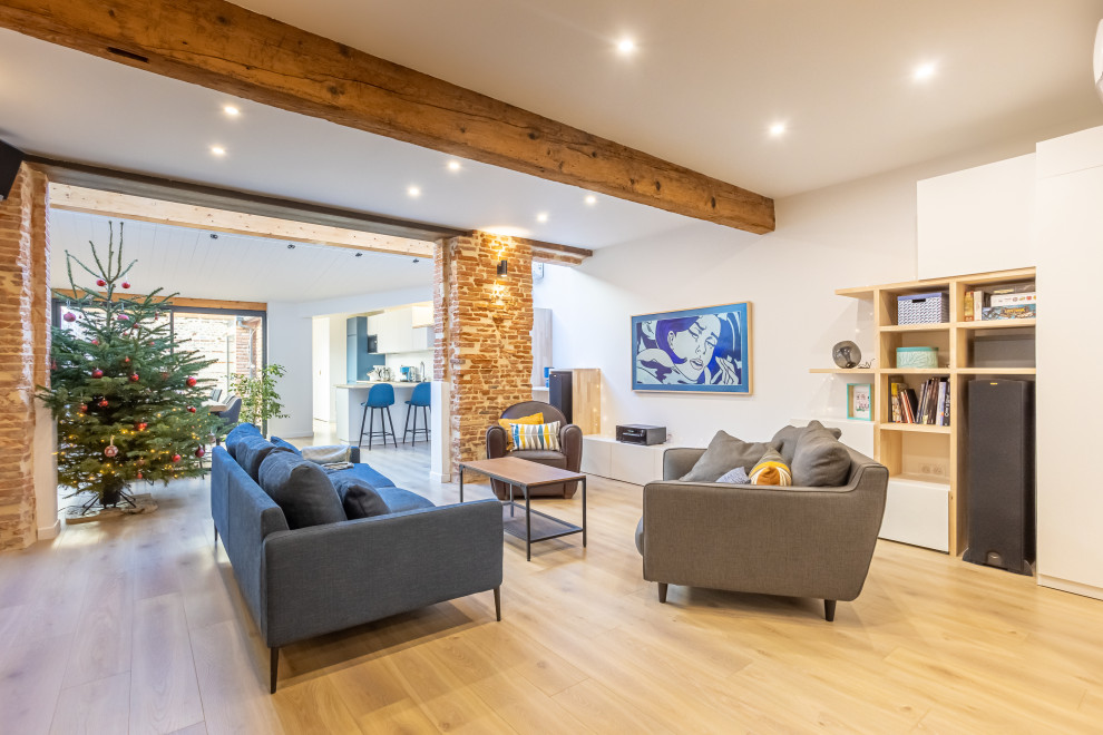 Photo of a large contemporary open concept living room in Toulouse with a library, white walls, light hardwood floors, no fireplace, a wall-mounted tv and exposed beam.
