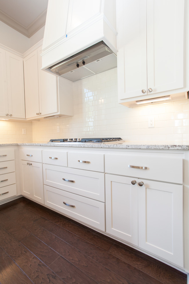 Photo of a mid-sized transitional l-shaped eat-in kitchen in New Orleans with raised-panel cabinets, white cabinets, marble benchtops, white splashback, ceramic splashback, stainless steel appliances, dark hardwood floors and with island.