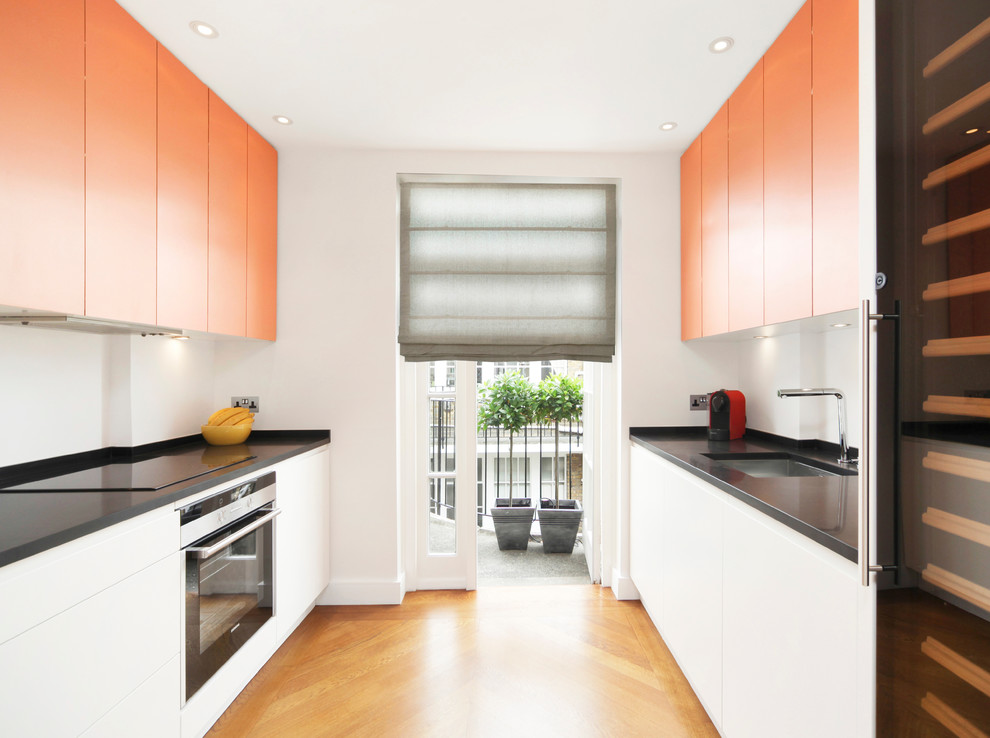 Inspiration for a mid-sized contemporary galley kitchen in London with flat-panel cabinets, white splashback, stainless steel appliances, light hardwood floors, no island, an undermount sink, orange cabinets and granite benchtops.