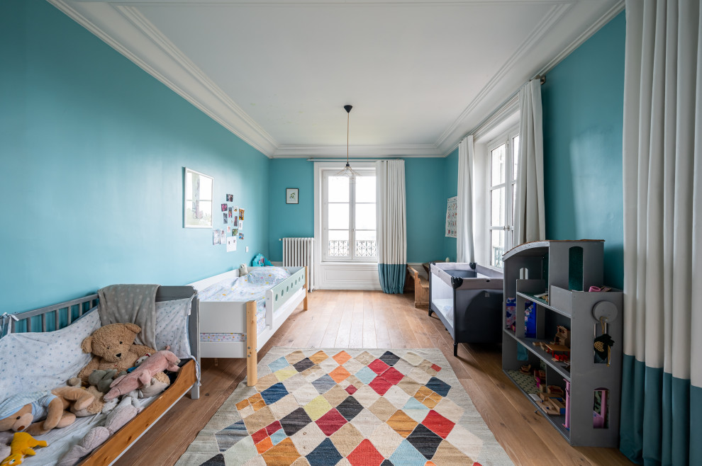 This is an example of a large contemporary gender neutral toddler’s room in Other with blue walls, light hardwood flooring, brown floors and exposed beams.