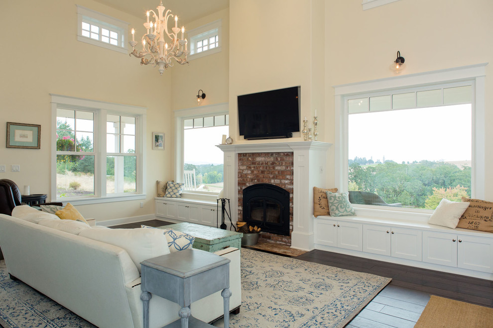Photo of a mid-sized country open concept living room in Portland with white walls, dark hardwood floors, a standard fireplace, a brick fireplace surround and a wall-mounted tv.