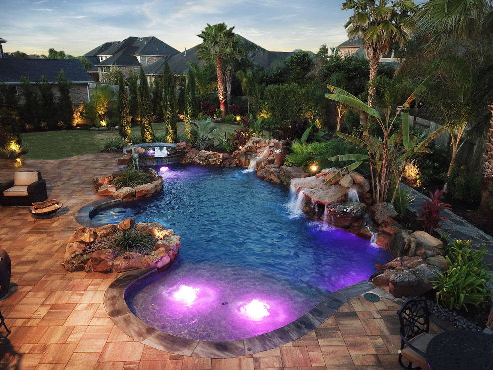Photo of a large traditional backyard custom-shaped pool in Houston with a hot tub and natural stone pavers.