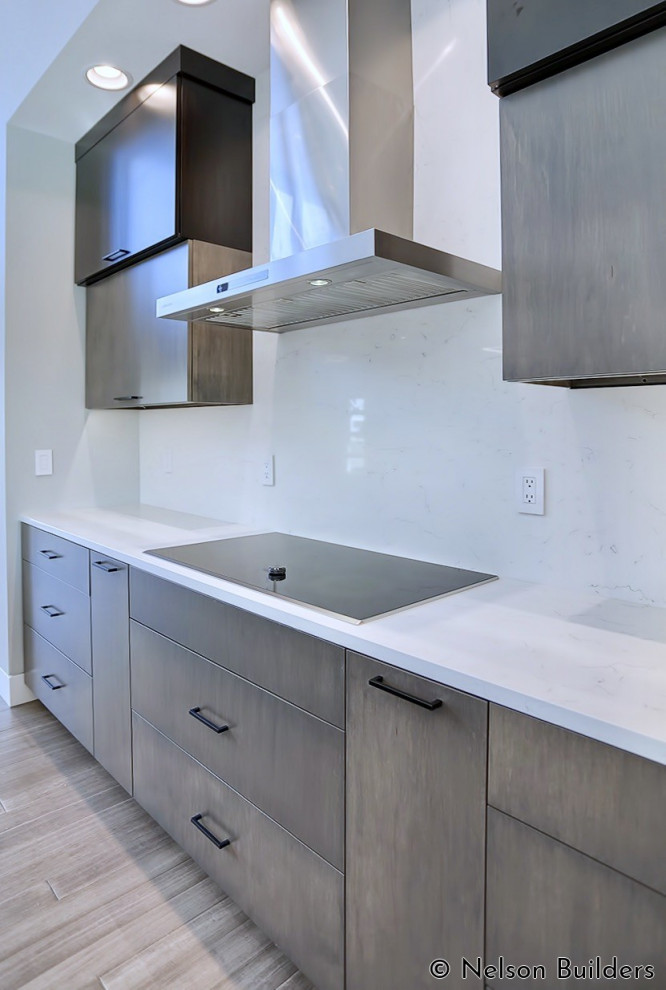 Photo of a mid-sized modern l-shaped open plan kitchen in Chicago with an undermount sink, flat-panel cabinets, medium wood cabinets, quartz benchtops, white splashback, engineered quartz splashback, stainless steel appliances, medium hardwood floors, with island, brown floor, white benchtop and vaulted.