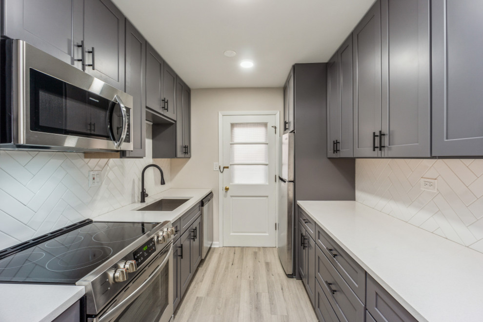 This is an example of a small farmhouse galley enclosed kitchen in Chicago with a built-in sink, recessed-panel cabinets, grey cabinets, white splashback, stainless steel appliances, vinyl flooring, no island, grey floors and white worktops.