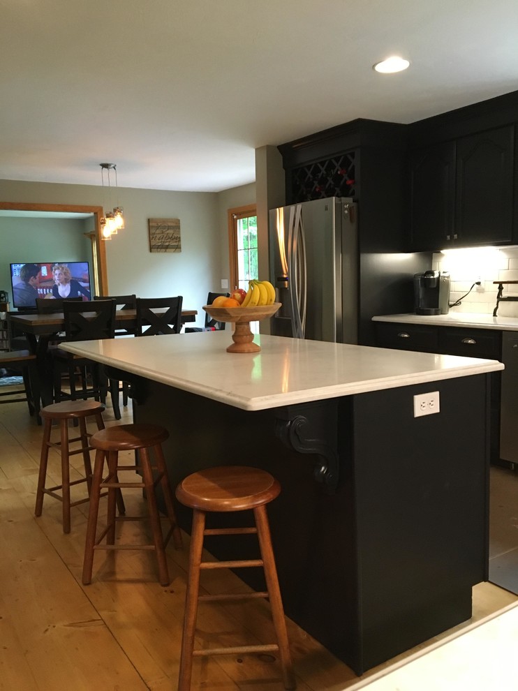 Example of a mid-sized transitional l-shaped light wood floor eat-in kitchen design in Boston with black cabinets, white backsplash, subway tile backsplash, stainless steel appliances, raised-panel cabinets, an island, marble countertops and a farmhouse sink