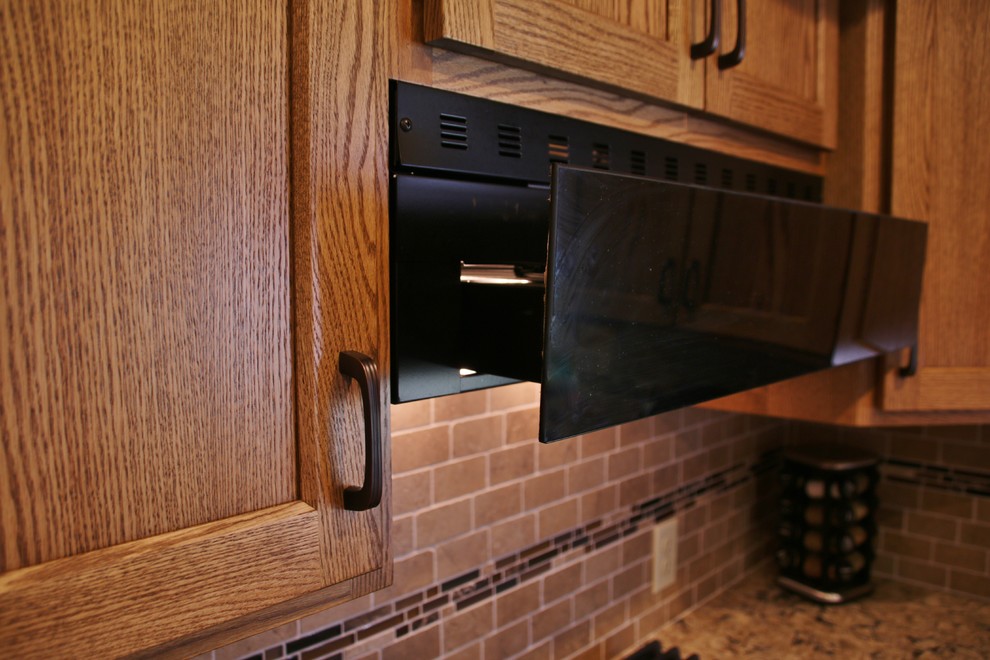 Mid-sized l-shaped eat-in kitchen photo with flat-panel cabinets, medium tone wood cabinets, quartz countertops, beige backsplash, black appliances and an island