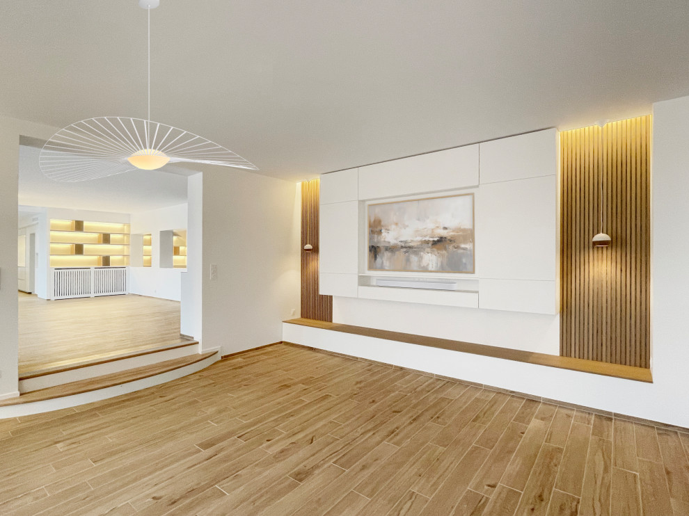 Cette image montre un très grand salon blanc et bois nordique ouvert avec une salle de réception, un mur blanc, parquet clair, un téléviseur encastré, boiseries et éclairage.