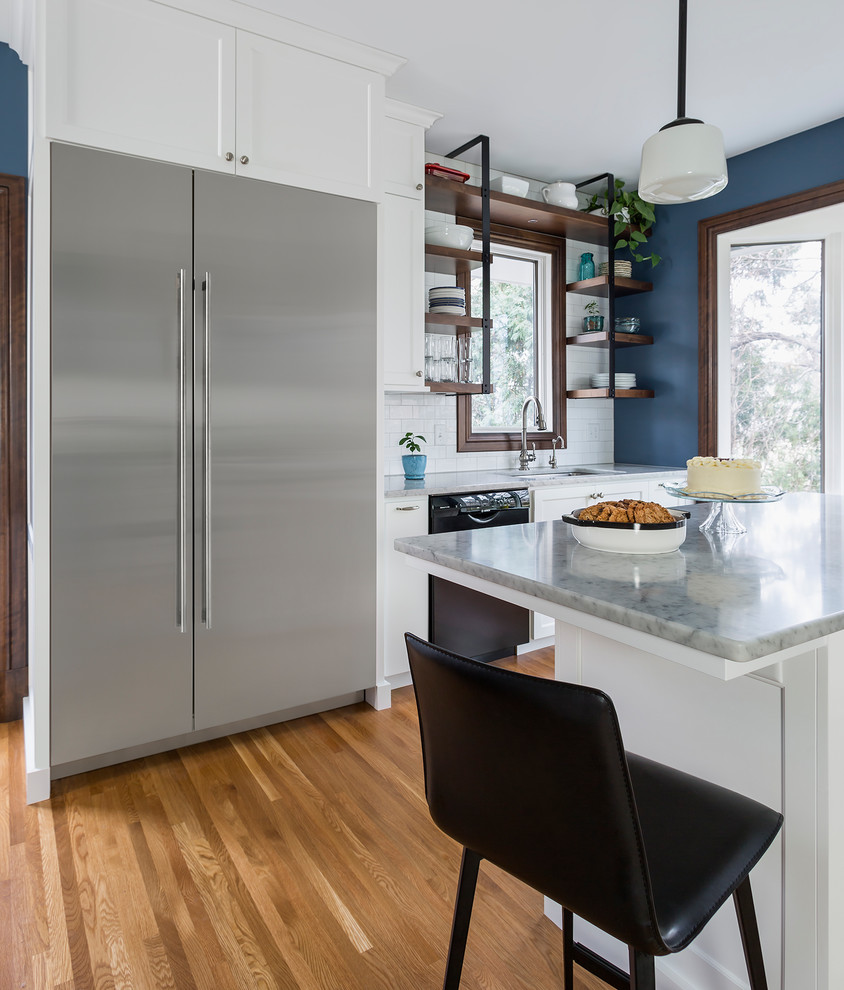 This is an example of a mid-sized traditional u-shaped separate kitchen in Minneapolis with an undermount sink, flat-panel cabinets, white cabinets, marble benchtops, white splashback, ceramic splashback, stainless steel appliances, medium hardwood floors, with island and brown floor.