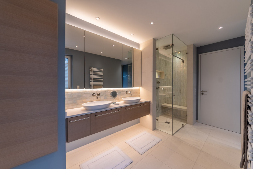 Duschbad mit Glasfronten, braunen Schränken, Einbaubadewanne, Eckdusche, Toilette mit Aufsatzspülkasten, beigen Fliesen, Steinfliesen, beiger Wandfarbe, Keramikboden, Aufsatzwaschbecken, beigem Boden, Schiebetür-Duschabtrennung, weißer Waschtischplatte, Duschbank, Doppelwaschbecken und freistehendem Waschtisch in Munich