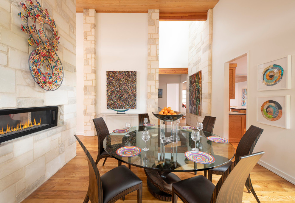 Mid-sized contemporary open plan dining in Dallas with white walls, medium hardwood floors, a two-sided fireplace, a stone fireplace surround, brown floor and wood.