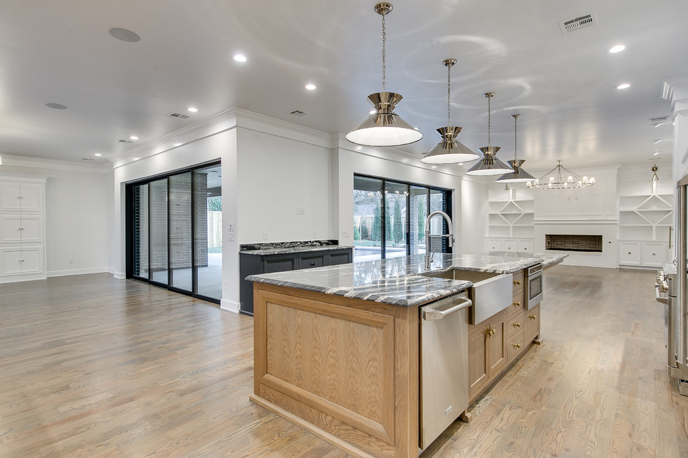 This is an example of an expansive modern kitchen in Oklahoma City with flat-panel cabinets, white cabinets, granite benchtops, black splashback, stone slab splashback, stainless steel appliances, medium hardwood floors, with island and black benchtop.