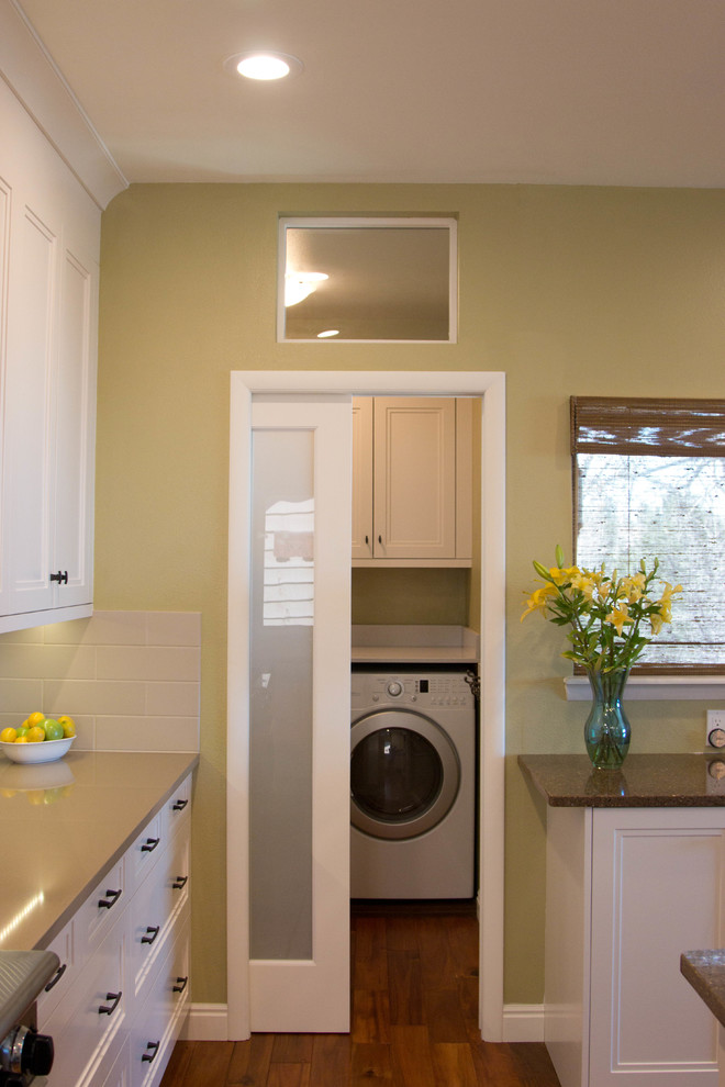Photo of a small transitional l-shaped laundry room in Denver with an undermount sink, white cabinets, quartz benchtops, beige splashback, cement tile splashback, medium hardwood floors and recessed-panel cabinets.