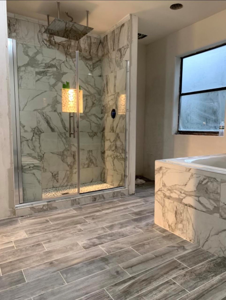 Photo of a master bathroom in Houston with a drop-in tub, a shower/bathtub combo, porcelain tile, wood-look tile, grey floor, a hinged shower door and a niche.