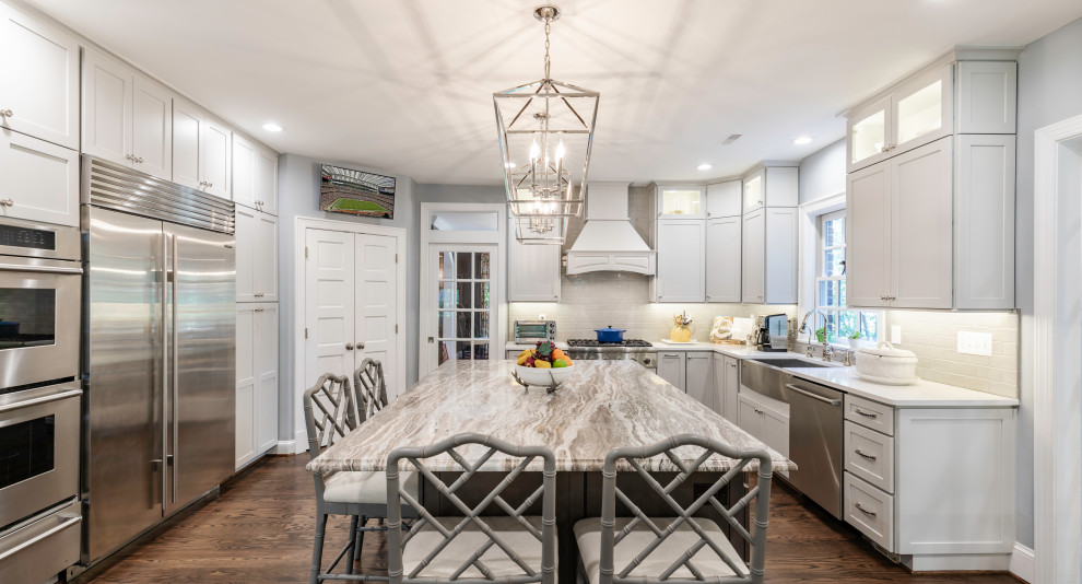 Mid-sized contemporary l-shaped eat-in kitchen in DC Metro with a farmhouse sink, beaded inset cabinets, white cabinets, white splashback, stainless steel appliances, with island, brown floor and white benchtop.