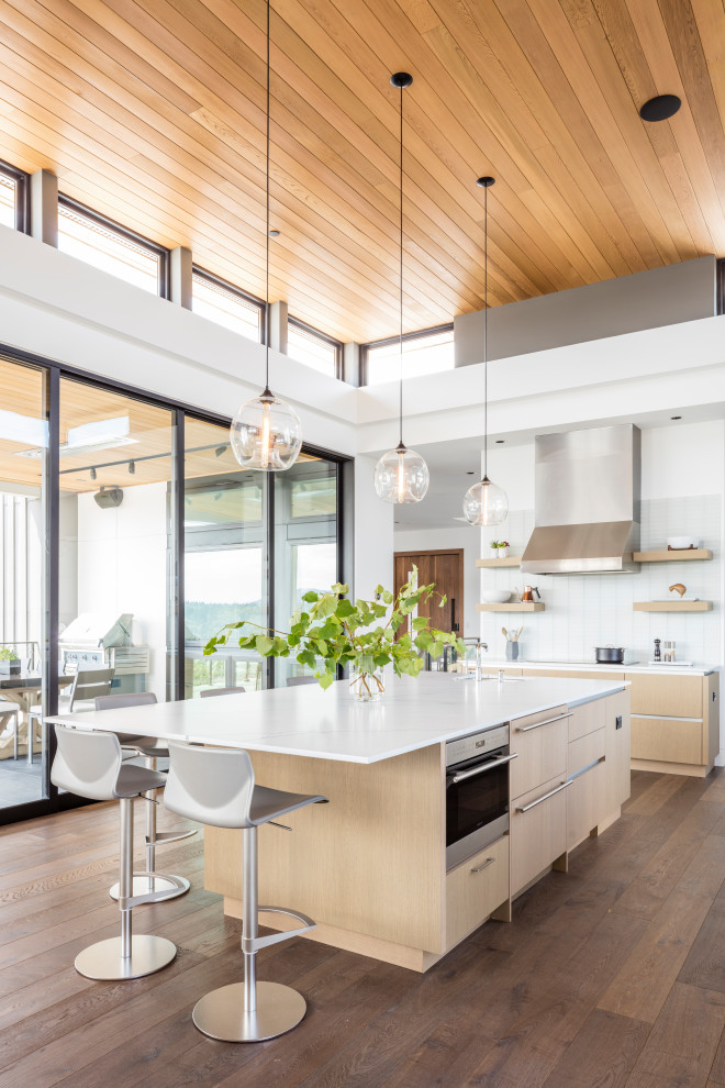 Design ideas for a large modern l-shaped open plan kitchen in Seattle with a farmhouse sink, flat-panel cabinets, white cabinets, marble benchtops, white splashback, glass tile splashback, panelled appliances, medium hardwood floors, with island, brown floor and white benchtop.