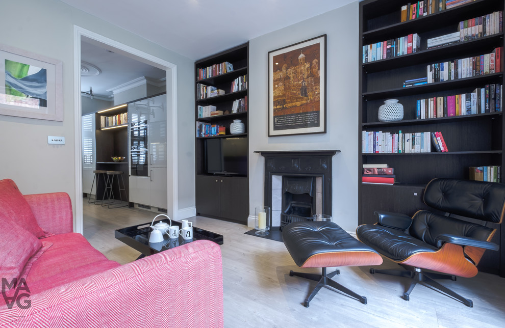 This is an example of a mid-sized contemporary open concept living room in London with a library, grey walls, light hardwood floors, a standard fireplace, a metal fireplace surround, a built-in media wall and grey floor.