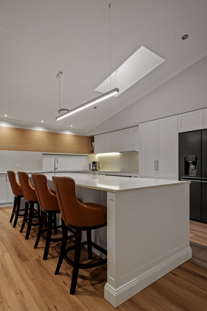 Inspiration for a large scandinavian l-shaped eat-in kitchen in Sydney with a double-bowl sink, shaker cabinets, white cabinets, quartz benchtops, white splashback, engineered quartz splashback, stainless steel appliances, vinyl floors, with island, brown floor and white benchtop.