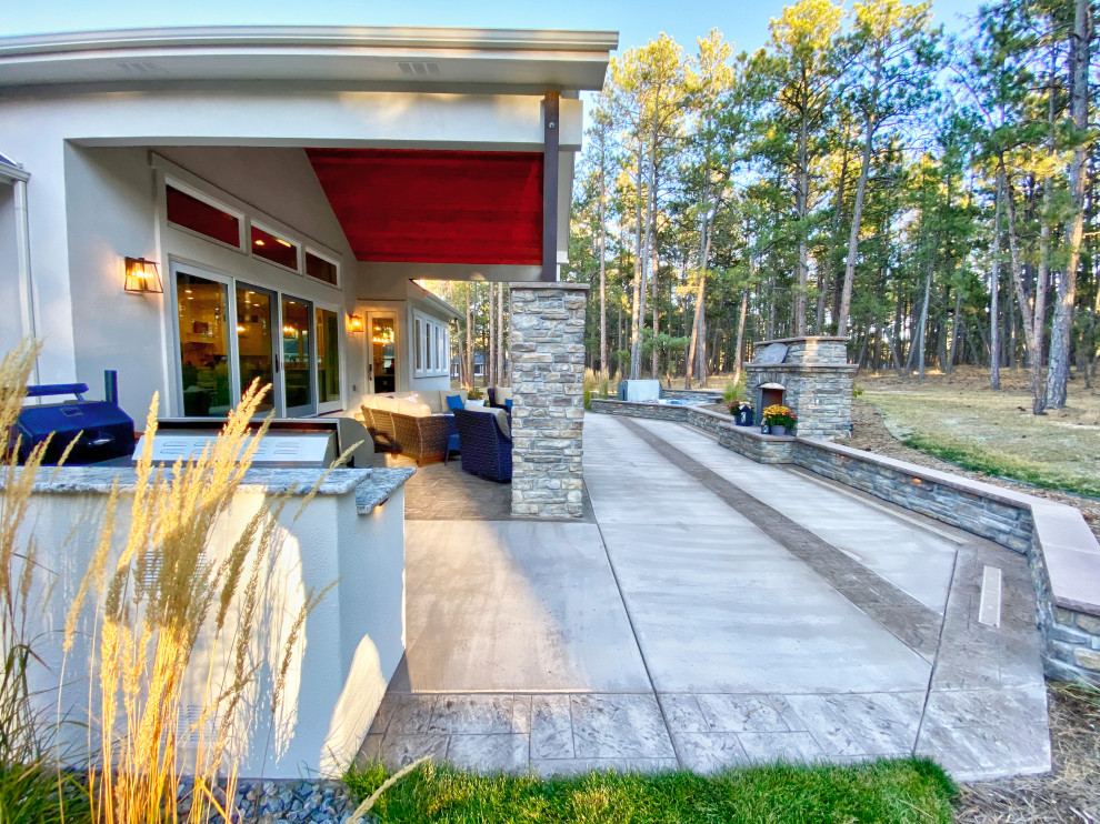 Foto di un grande patio o portico tradizionale dietro casa con un caminetto, cemento stampato e un tetto a sbalzo