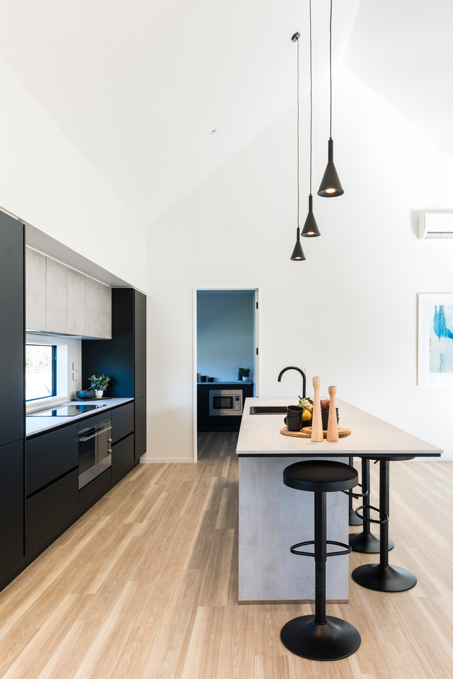 Photo of a mid-sized modern galley kitchen pantry in Christchurch with a drop-in sink, flat-panel cabinets, black cabinets, laminate benchtops, white splashback, window splashback, stainless steel appliances, laminate floors, with island and brown floor.