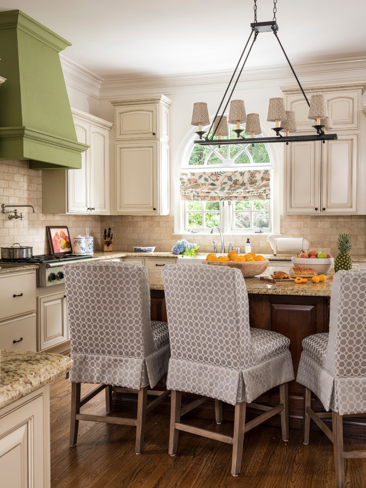 This is an example of a traditional kitchen in Atlanta with a farmhouse sink, raised-panel cabinets, beige cabinets, beige splashback, subway tile splashback, stainless steel appliances, dark hardwood floors, with island, brown floor and multi-coloured benchtop.