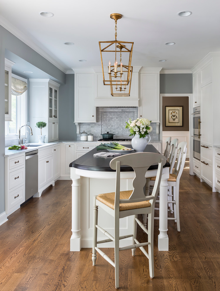 This is an example of a large traditional u-shaped open plan kitchen in Minneapolis with an undermount sink, white cabinets, marble benchtops, stone tile splashback, panelled appliances, medium hardwood floors and with island.