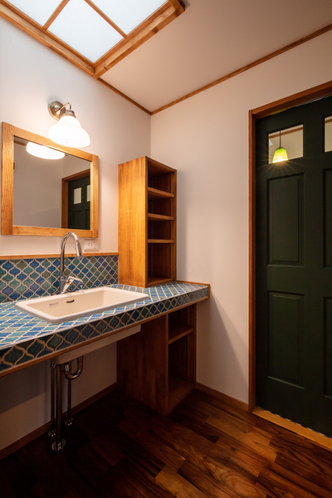 This is an example of a country powder room in Other with turquoise cabinets, multi-coloured tile, mosaic tile, white walls, dark hardwood floors, an undermount sink, tile benchtops, brown floor, turquoise benchtops, a built-in vanity, wallpaper and wallpaper.