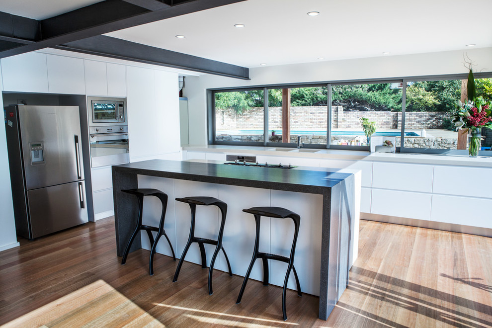 Inspiration for a large contemporary l-shaped open plan kitchen in Sydney with an undermount sink, flat-panel cabinets, white cabinets, solid surface benchtops, stainless steel appliances, medium hardwood floors and with island.