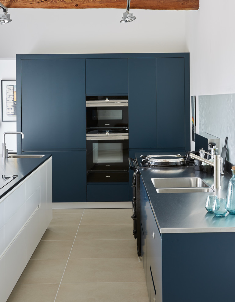 Design ideas for a contemporary u-shaped eat-in kitchen in London with a drop-in sink, flat-panel cabinets, blue cabinets, solid surface benchtops, grey splashback, stainless steel appliances, medium hardwood floors, multiple islands and black benchtop.