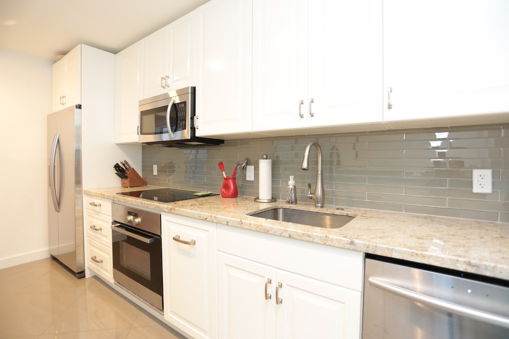 Inspiration for a small transitional galley separate kitchen in Miami with an undermount sink, raised-panel cabinets, white cabinets, granite benchtops, grey splashback, glass tile splashback, stainless steel appliances, porcelain floors and no island.