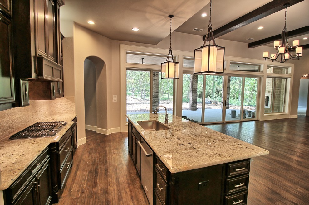 Photo of a large transitional l-shaped open plan kitchen in Dallas with an undermount sink, raised-panel cabinets, dark wood cabinets, granite benchtops, white splashback, stone tile splashback, stainless steel appliances, medium hardwood floors, with island and brown floor.
