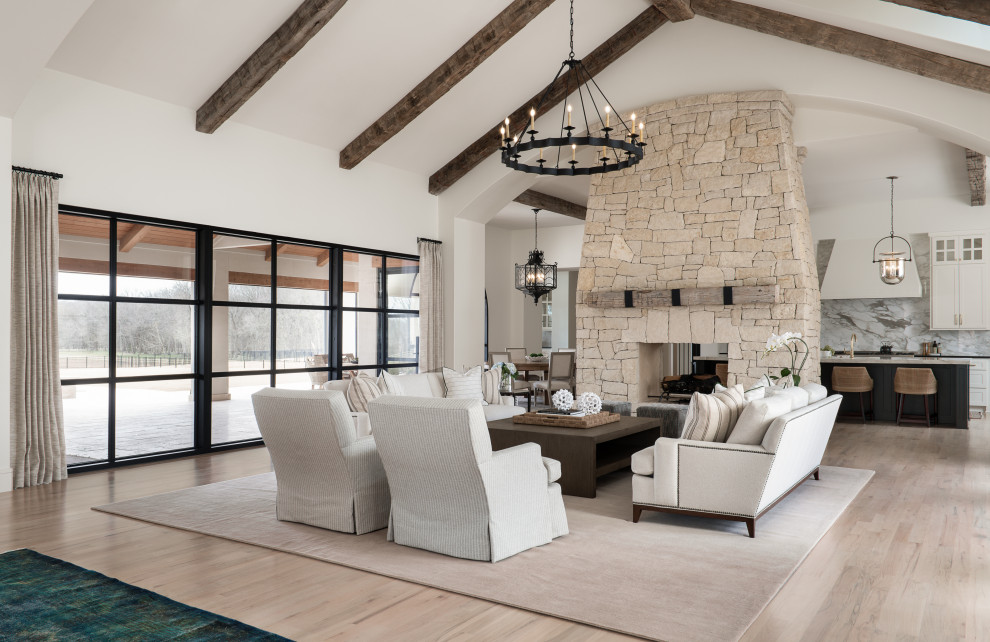 Huge transitional open concept light wood floor and exposed beam living room photo in Minneapolis with white walls, a two-sided fireplace and a stacked stone fireplace