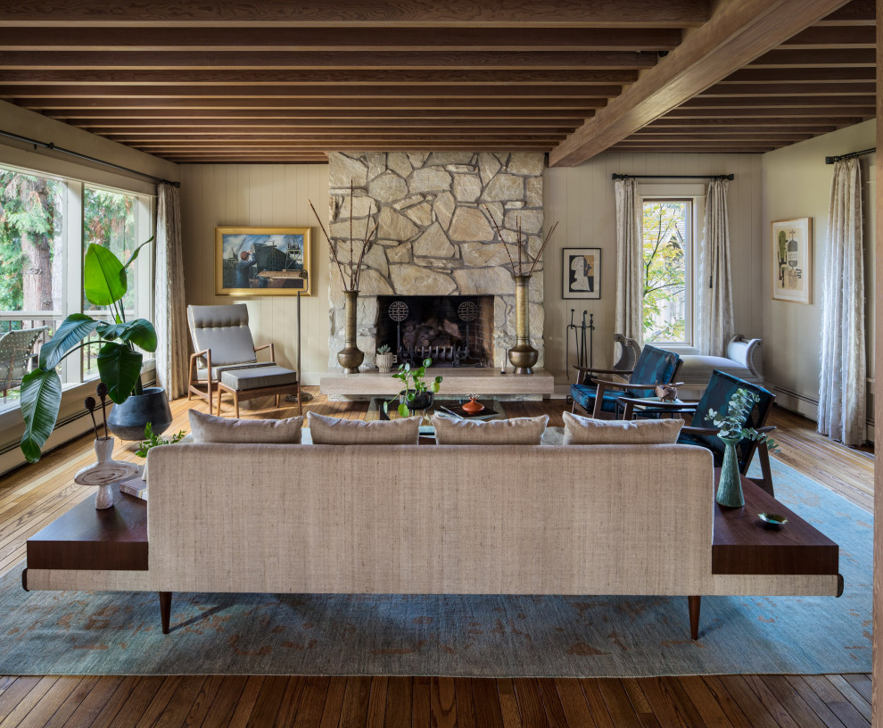 Large midcentury formal open concept living room in Portland with a stone fireplace surround, brown floor, beige walls, medium hardwood floors, a standard fireplace, exposed beam and planked wall panelling.