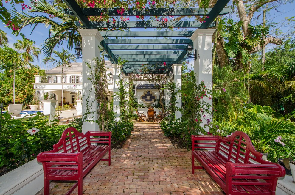 This is an example of a tropical patio in Miami with brick pavers and a pergola.