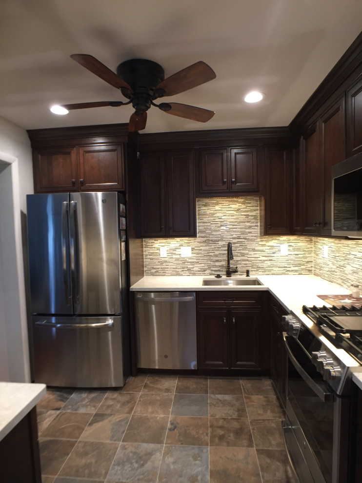 Photo of a medium sized traditional l-shaped enclosed kitchen in New York with a submerged sink, recessed-panel cabinets, dark wood cabinets, engineered stone countertops, beige splashback, matchstick tiled splashback, stainless steel appliances, slate flooring, no island, brown floors and beige worktops.