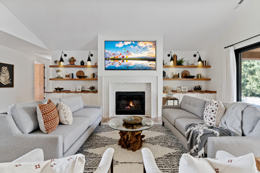 This is an example of a large country open concept living room in Portland with white walls, laminate floors, a standard fireplace, a brick fireplace surround, a built-in media wall, brown floor and vaulted.