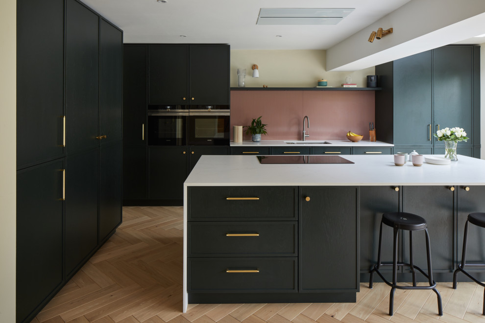 Large contemporary l-shaped eat-in kitchen in Kent with recessed-panel cabinets, green cabinets, quartz benchtops, pink splashback, glass sheet splashback, stainless steel appliances, with island and white benchtop.