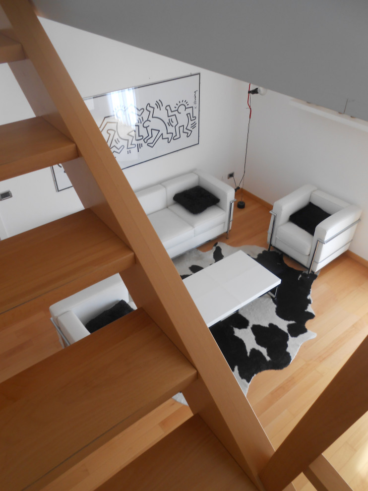 Esempio di un soggiorno design aperto con pareti bianche, parquet chiaro e TV a parete