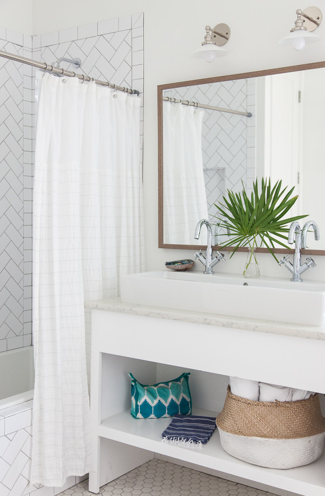 This is an example of a beach style bathroom in Miami with open cabinets, white cabinets, a drop-in tub, a shower/bathtub combo, white tile, white walls, a trough sink and a shower curtain.