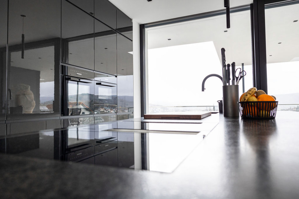 Inspiration for a contemporary galley eat-in kitchen in Frankfurt with an undermount sink, granite benchtops, grey splashback, black appliances, ceramic floors, with island, grey floor and grey benchtop.